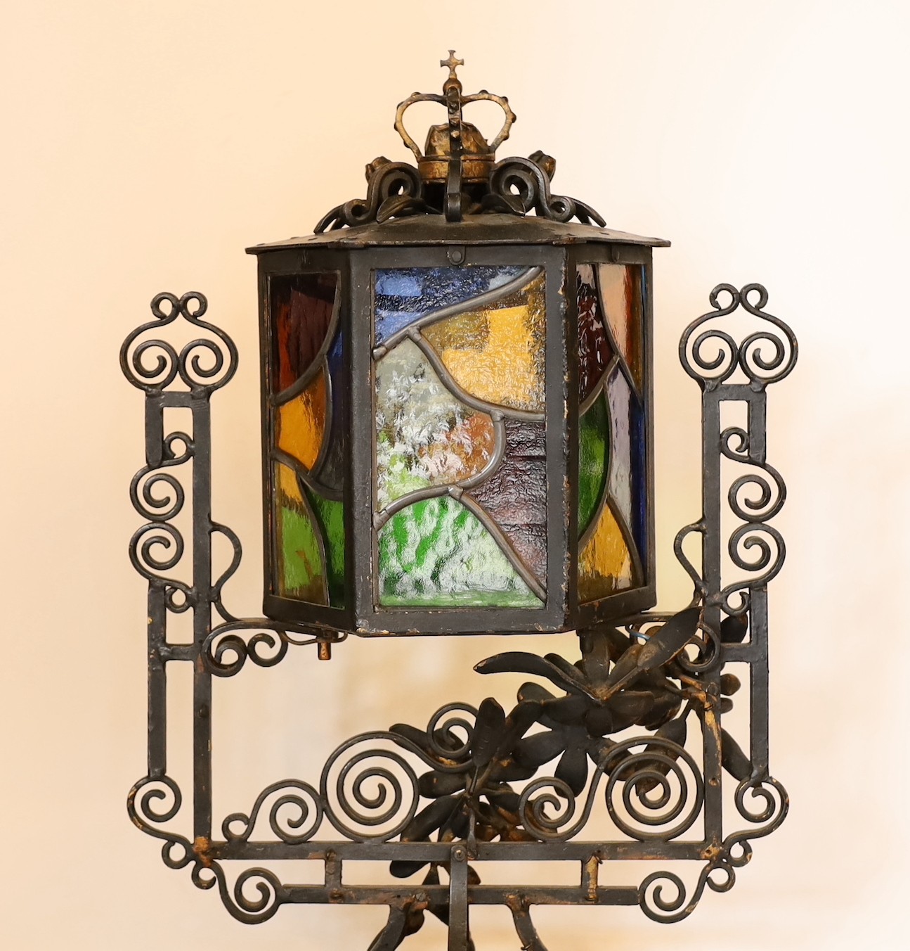 An early 20th century English wrought iron and stained-glass hexagonal lantern style table lamp with crown finial and parcel built black painted finish, height 50cm. width 32cm